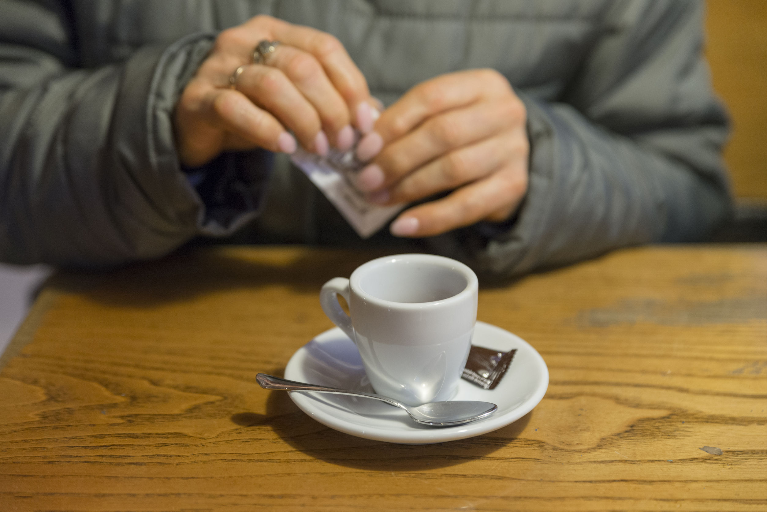 92999253 - picture of a cup of coffee drank at the bar, behind the cup a sugar sachet is spreading.